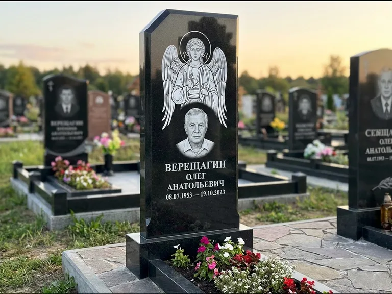 Памятник с гравировкой иконы: стела с резным навершием и нимбом в золоте — гравировка образа Спасителя, высокие разросшиеся туи полукругом, работа «Мельникова» в Калининграде