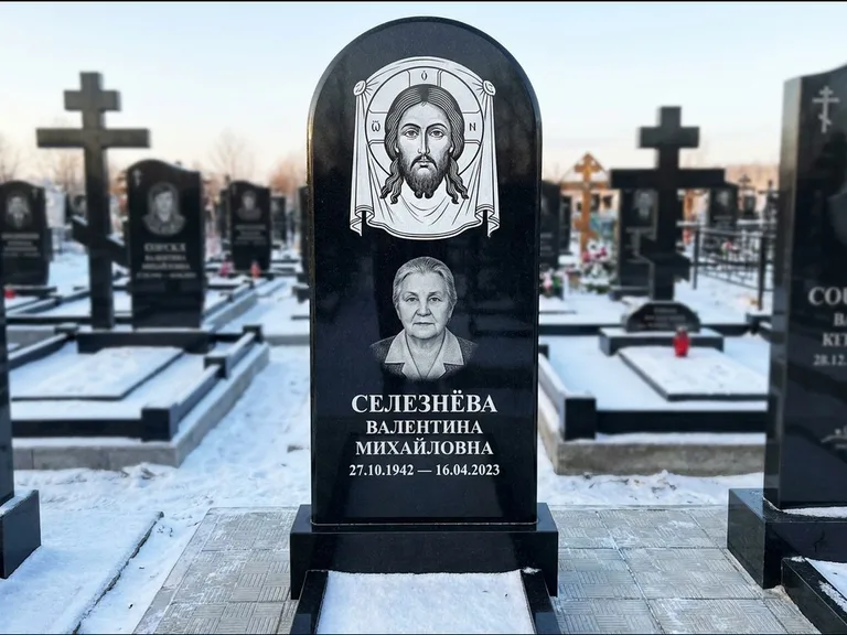 Памятник с гравировкой иконы: небольшая скромная одиночная стела с именной иконой — золочёный нимб на образе, аккуратный участок с газоном, работа «Ковалёв» в Калининграде