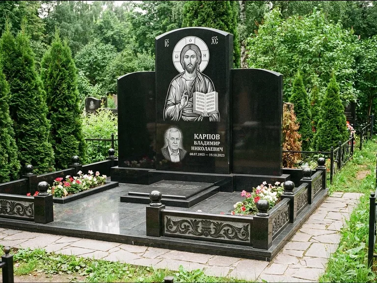 Памятник с гравировкой иконы: широкая панорамная стела с золочёным нимбом — гравировка образа Матроны Московской, цветник с белыми хризантемами, работа «Мельникова» в Калининграде