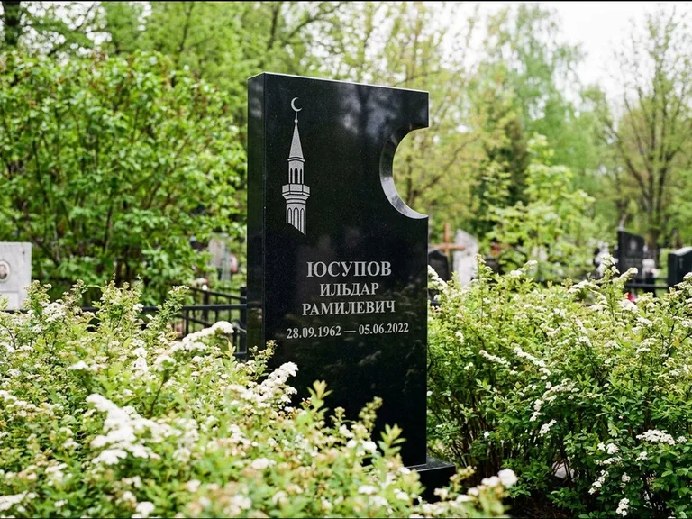 Мусульманский памятник с гравировкой мечети: стела с боковым вырезом в форме полумесяца — гравировка минарета с полумесяцем, низкие кусты спиреи в цвету, работа «Юсупов» в Калининграде